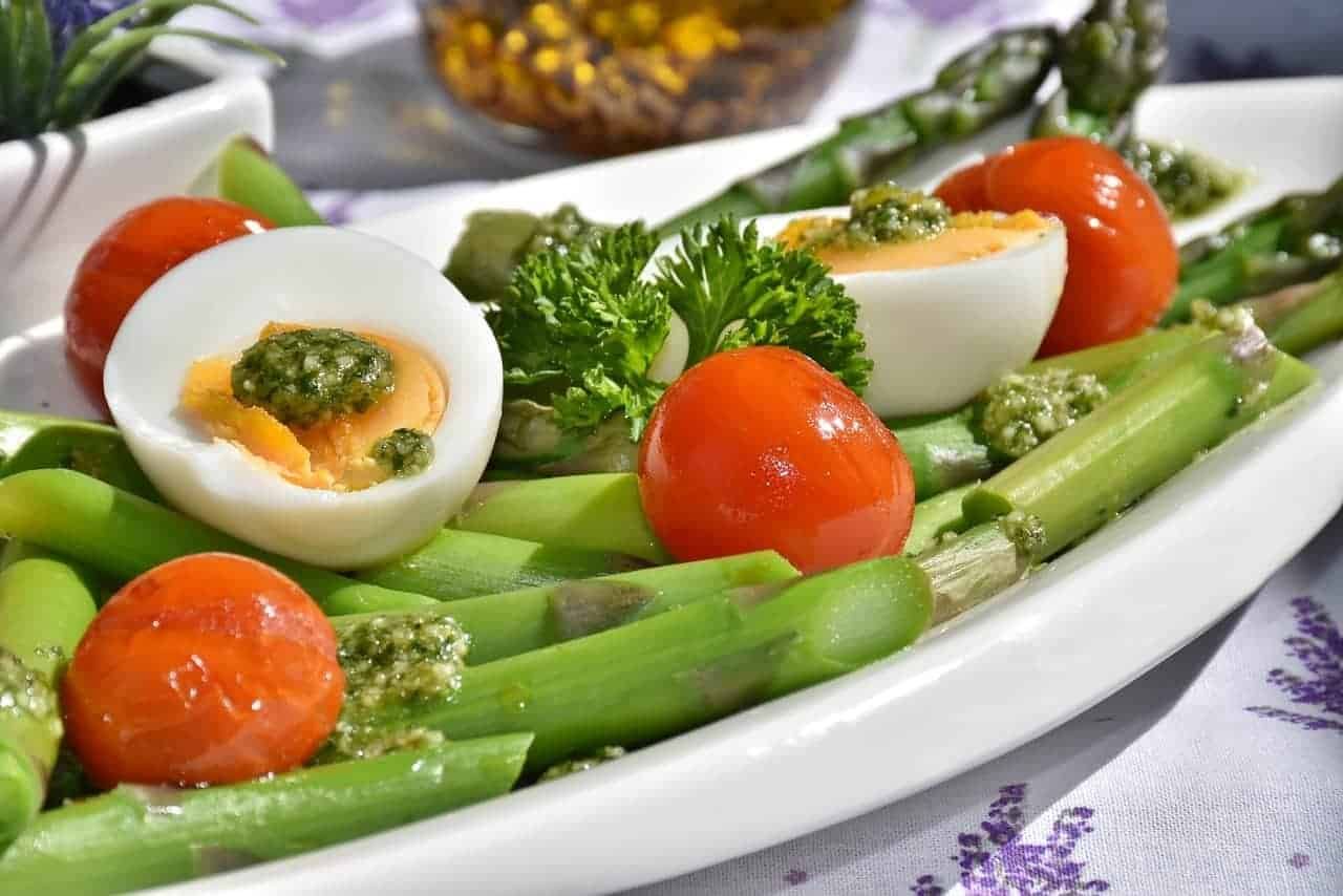 Ein weisser Teller mit Spargeln, Tomaten, Petersilie, Eiern und Pesto: Dies stellt aus Sicht der Ernährungspyramide der Schweiz, ein gesundes Menu dar.