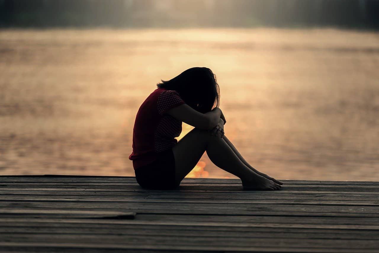 Junge Frau sitzt auf einem Steg an einem See im Sonnenuntergang. Eine von Natur aus entspannende Umgebung ermöglicht es ihr, komplett relaxed da zu sitzen.