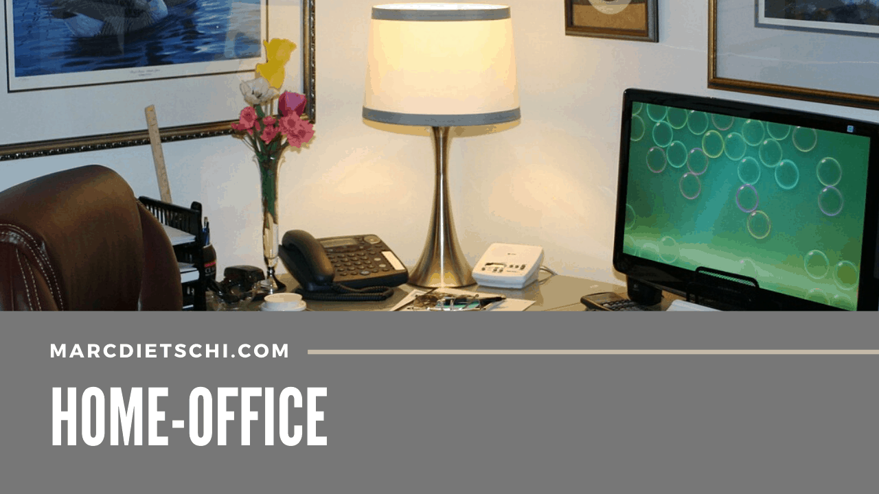 Pult, Computer, Telefon und Lampe im Home-Office. Es sind auch noch Blumen, Taschenrechner und Anrufbeantworter zu sehen.