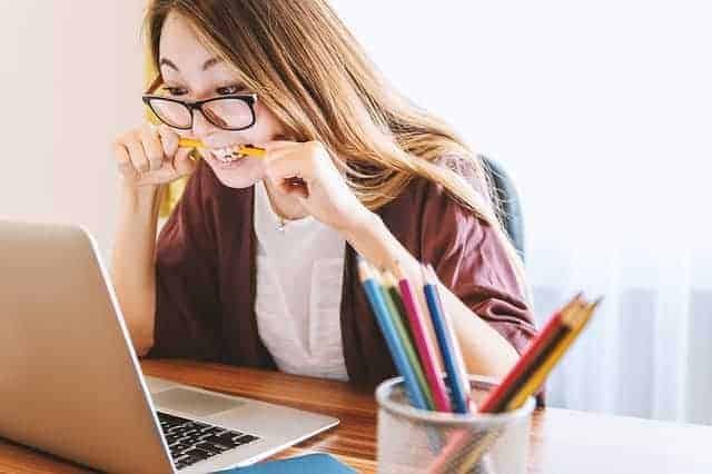 Frau versucht eine Rede zu schreiben am, Laptop und beisst dabei auf einen Bleistift.