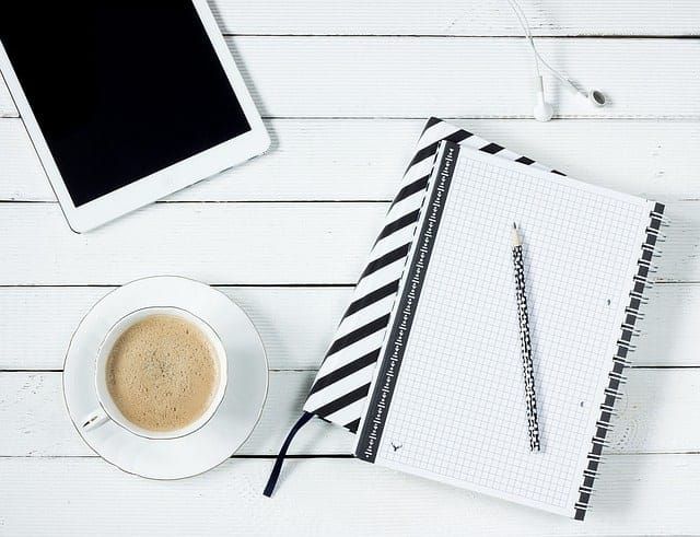 Mit Tablet, Kaffe und Notizblock auf eine Rede vorbereiten.