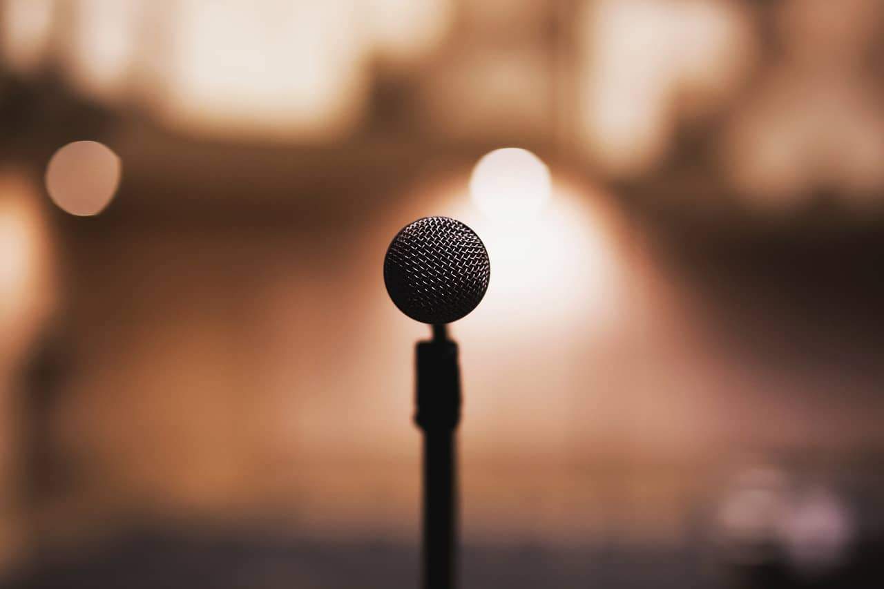 Ein Mikrofon, wie man es sieht, wenn man Keynote Speaker ist und vor vielen Leuten ein Referat hält. Im Hintergrund ist das Rampenlicht zu sehen.