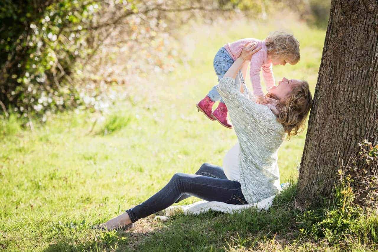 Eine Frau im Park, welche eine kleine süsse Tochter in die Luft hält und lacht. Klar ersichtlich ist, dass sie schwanger ist!