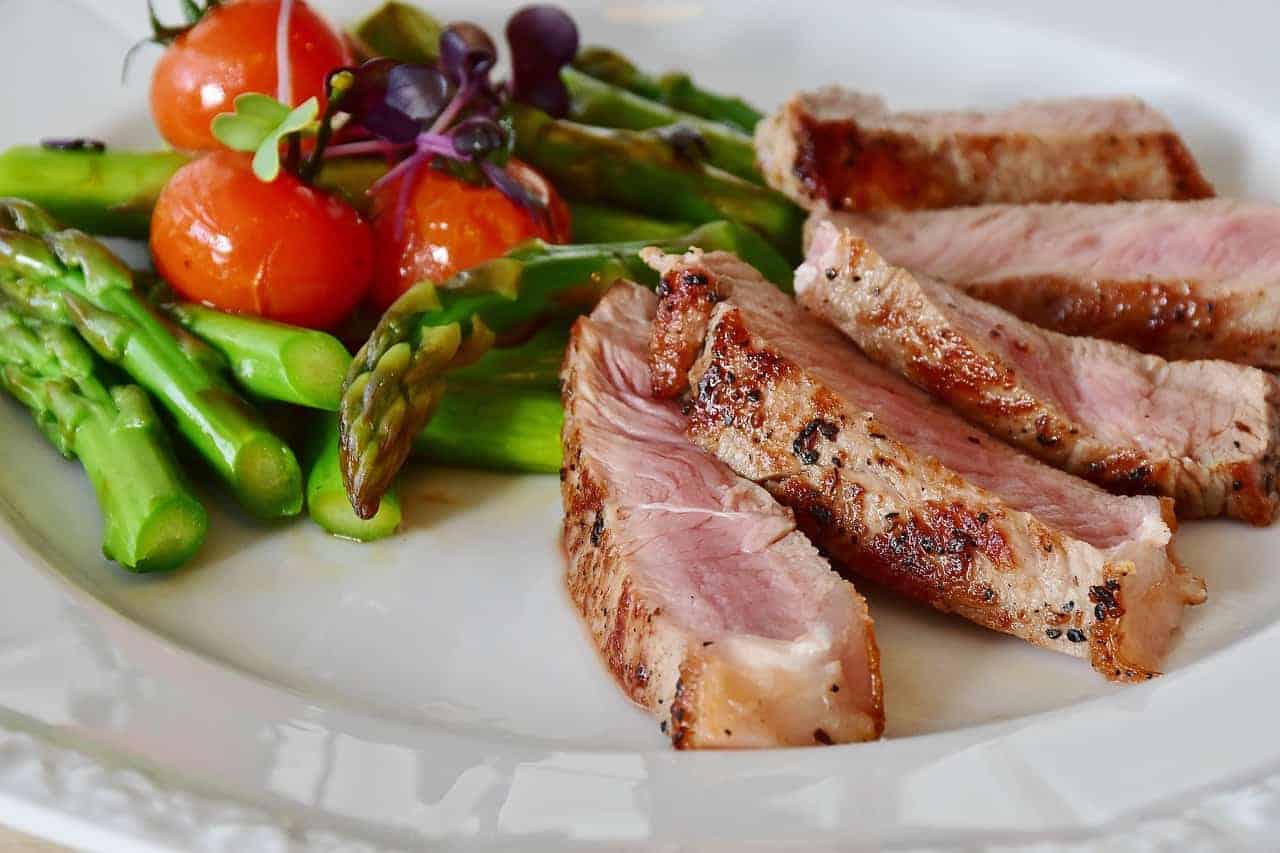 Appetitliches Steak mit gegrillten Spargeln und buntem Gemüse auf einem Teller, angerichtet für eine ausgewogene Mahlzeit.