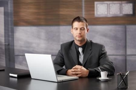Ein Mann in sitzender Meditation im Büro vor einem Notebook.