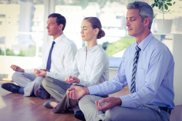 Drei im Business-Style gekleidete Personen in tiefer Meditation am Boden sitzend.
